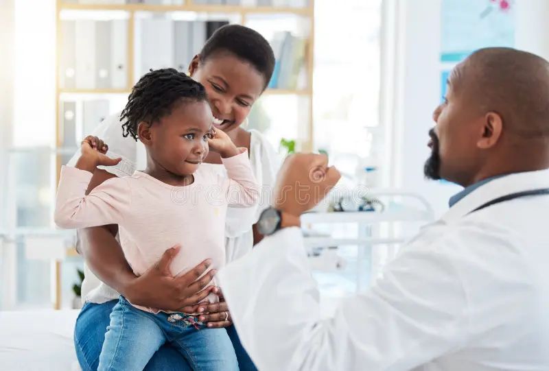 Doctor playfully examining a young child held by their mother during a wellness visit
