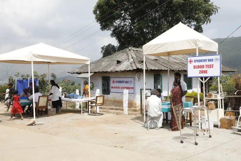 Outdoor NGO health camp with white tents, clinicians, and a blood test zone serving a rural community